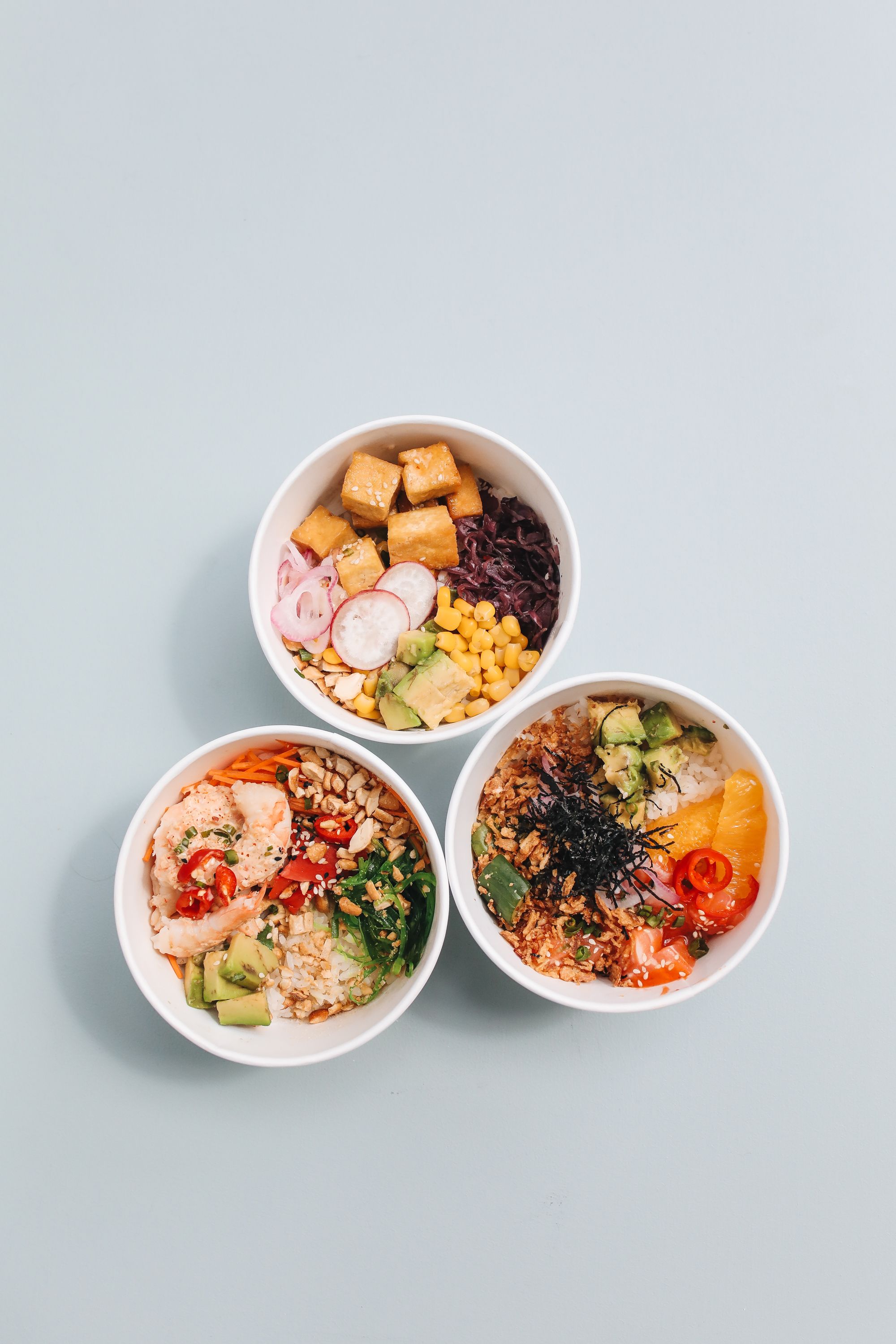 Three colorful grain bowls with avocado, corn, tofu, and greens